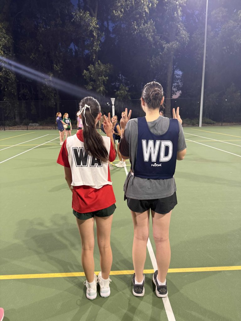 Two girls at the pregrading netball evening for Dynamites give a peace sign,